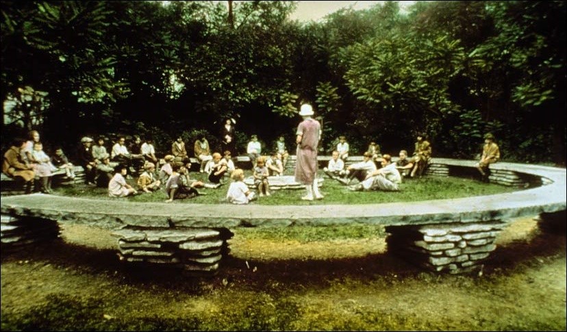 Image of children sitting in a circle on stone benches in nature.