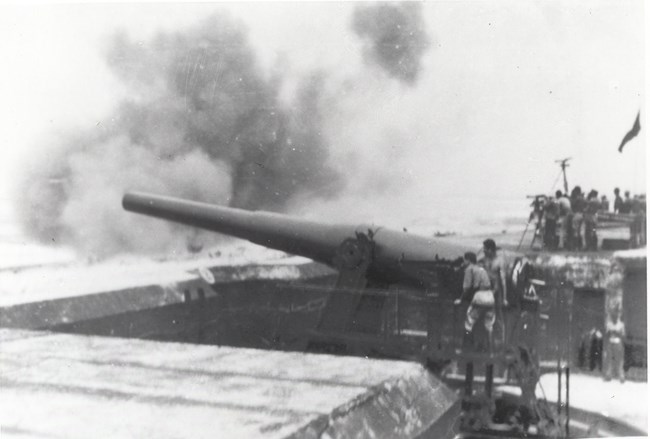 Black and white photo of a large steel cannon firing.