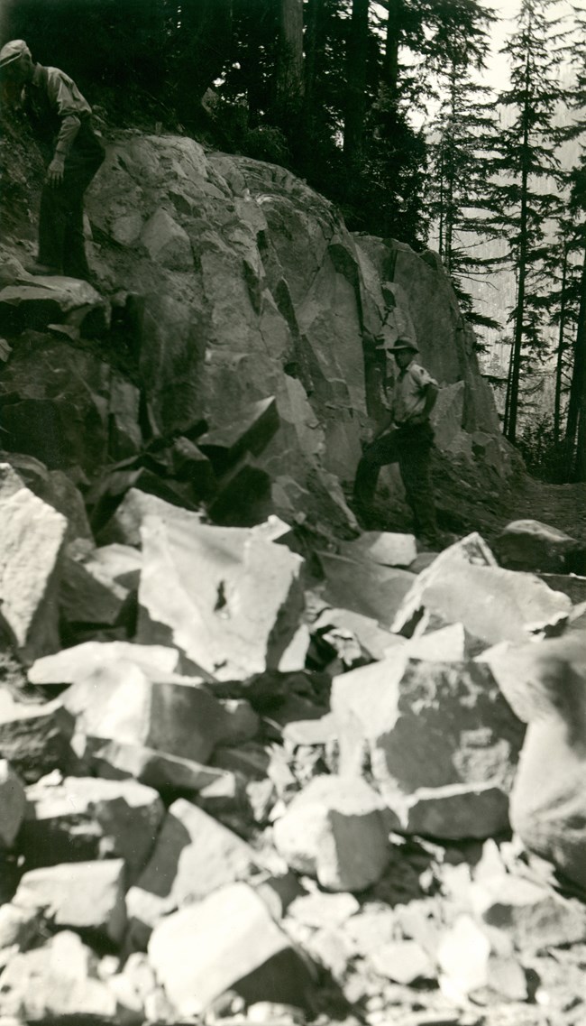 A man working at road construction along the Carbon River with rocks in the foreground.