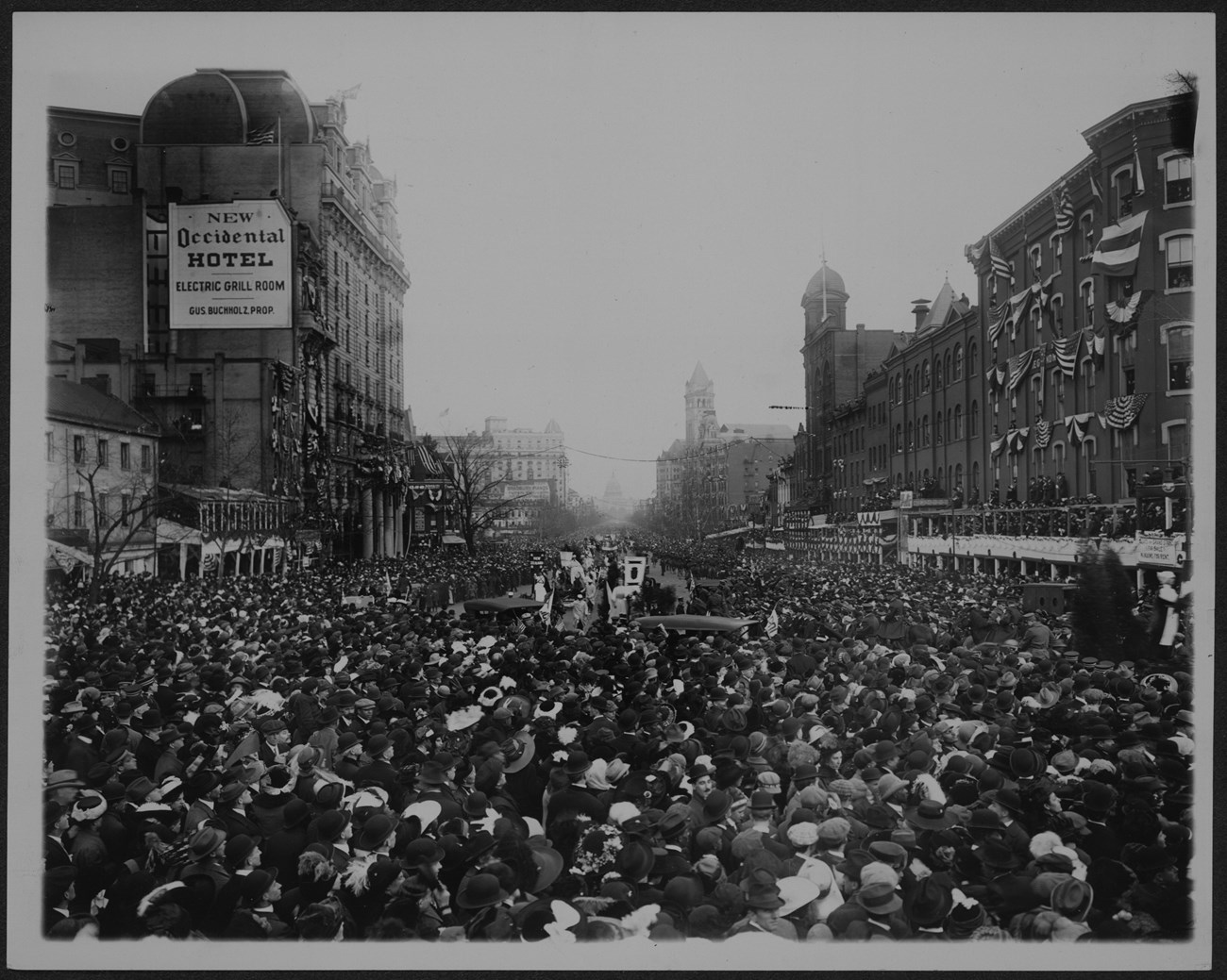 Photograph of suffrage procession surrounded by huge crowds in the street.