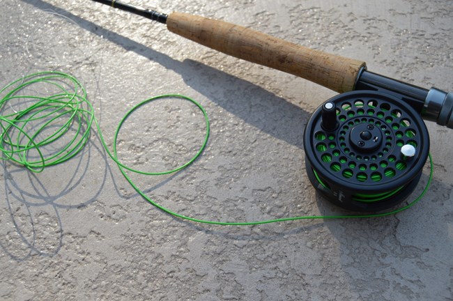 close up of fly fishing rod, reel, and line on cement