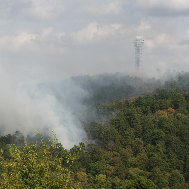 Smoke from a prescribed fire rises. The mountain observatory tower is at the top of the mountain.