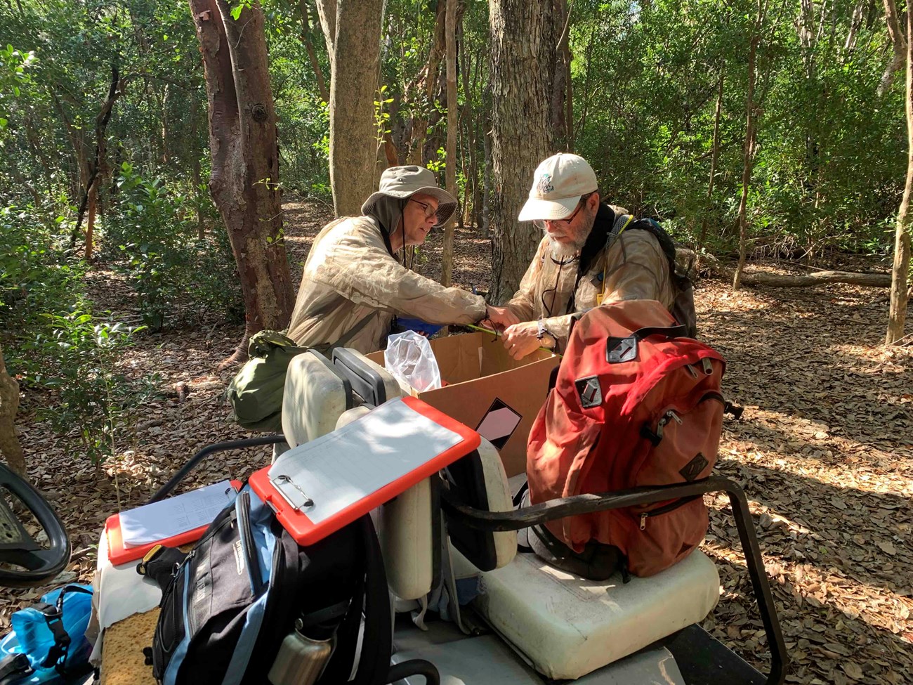 Two researchers sifting through field equipment, including backpacks, clipboards, and data sheets, that are in a vehicle.