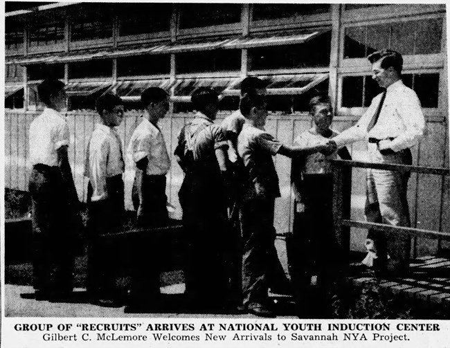 black and white photo of a group of boys lined up to shake the hand or a man in a suit