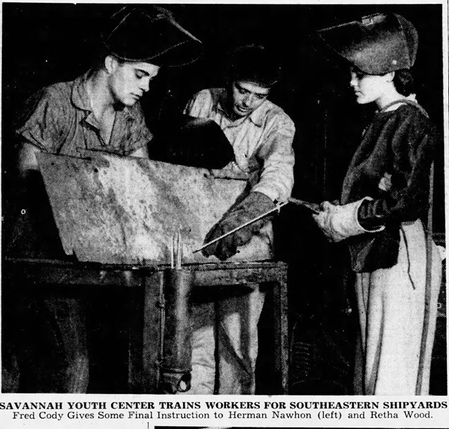 Black and white photo of two youths wearing welding masks being trained on metal work by an adult male