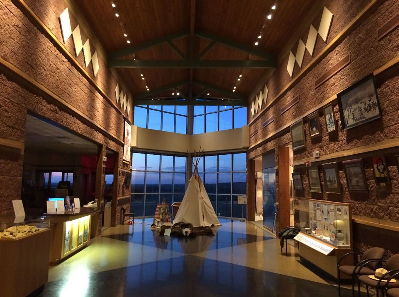 Inside a long building with a tipi at the end in front of a large window.