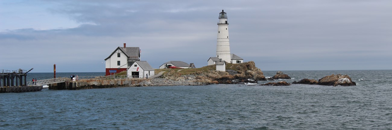 A white lighthouse on a small rocky island surrounded by blue ocean water