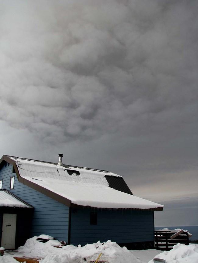 A cloud of volcanic ash from Redoubt seen above a house in the winter.