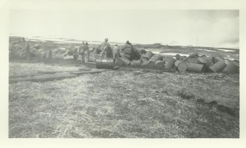 Black and white photo of men rolling barrels up an incline