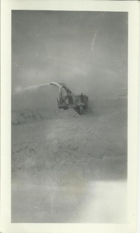 Black and white photo of a large snow plow in a snow bank