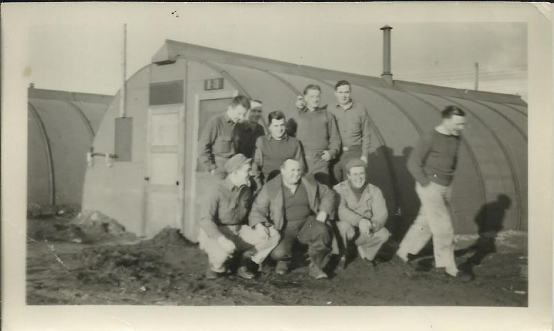 Black and white photo of men posing in front of a quonset hut