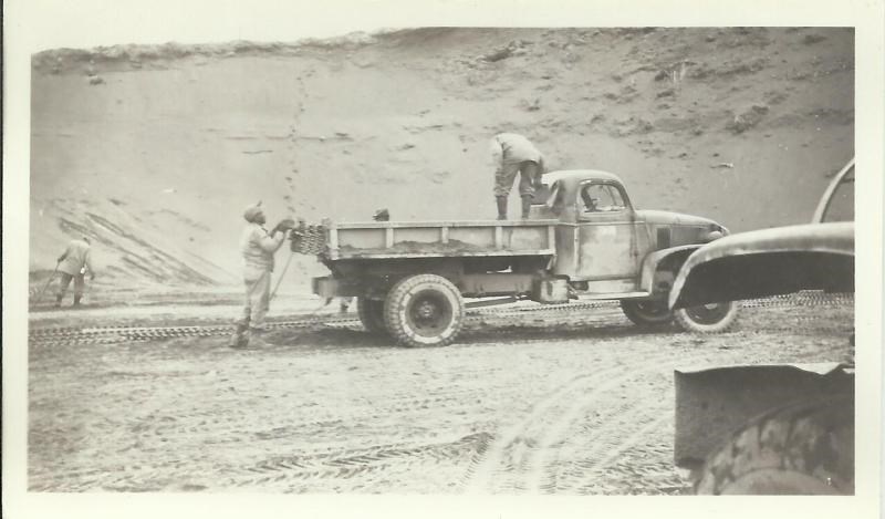 Black and white photo of men unloading wire mats from a truck with an earth bank behind them.