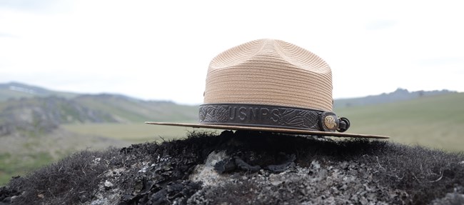 A NPS flat hat sits on a rock covered in lichen.