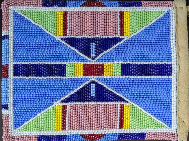 a Crow nation beaded pouch made from deerskin with triangular designs in bright blue, light green, pink, yellow, and navy