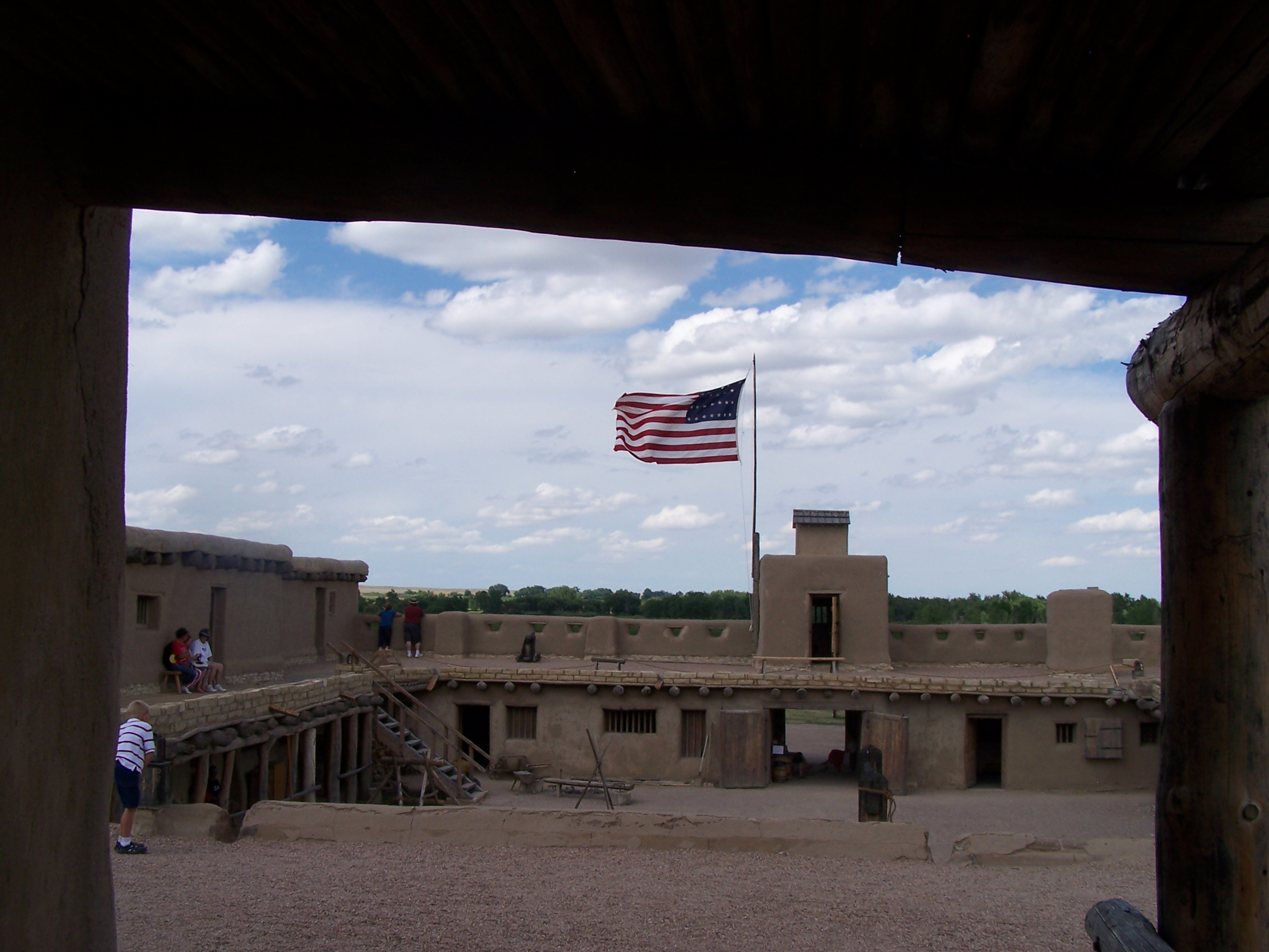 A historic American flag flies from a wooden pole on an adobe fort.