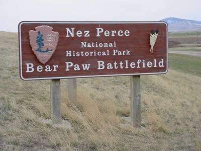 Wooden sign with  the National Park Service Arrowhead logo and the words "Nez Perce National Historical Park Bear Paw Battlefield" carved into it.