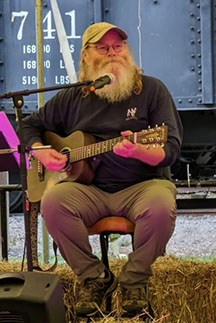 A musician sitting on a stool playing a guitar performing.