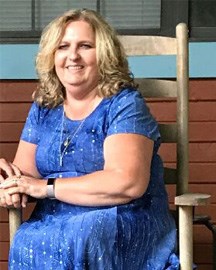 A woman with blonde hair in a blue dress sitting in a rocking chair.