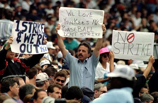 a crowd of people holding signs, with one man clearly in the center, wearing a blue shirt and holding a sign