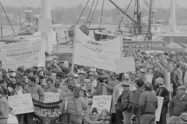 a group of people holding signs and protesting at a dock with ships in the background