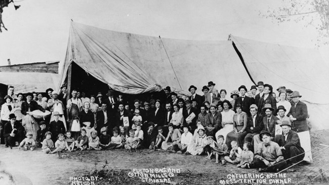 a large group of men, women, and children in front of a large tent