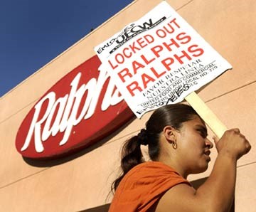 a woman with a ponytail holding a picket sign outside of a ralph's grocery store