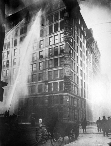 a tall building on fire being sprayed with large hoses as people watch in the street