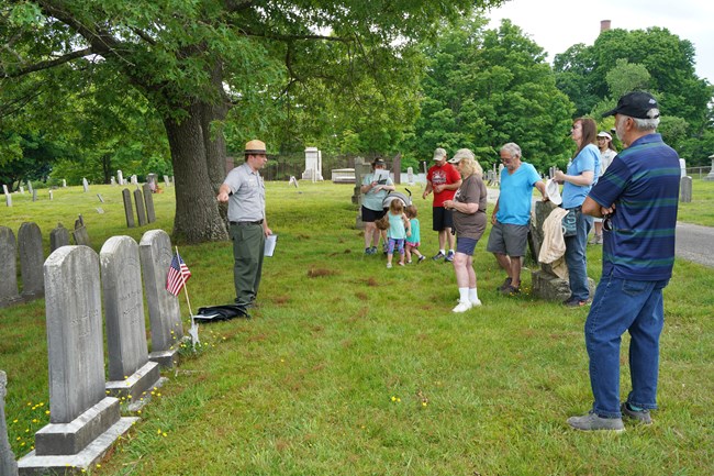 Park Ranger stands next to row of gravestones pointing while group of people listen