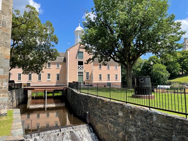 Waterway with waterfall in foreground and 2 1/2 story peach-colored wooden building in background
