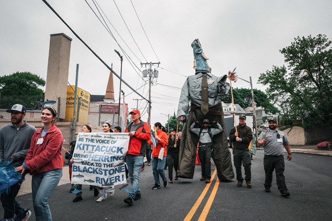 Group of people walking down the street. One wearing a giant ranger costume with fish for a head