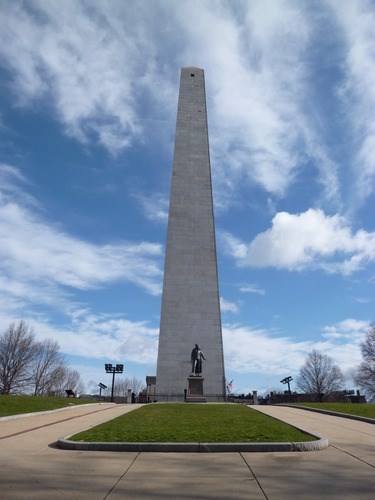 white granite obelisk against a blue sky with streaks of white clouds