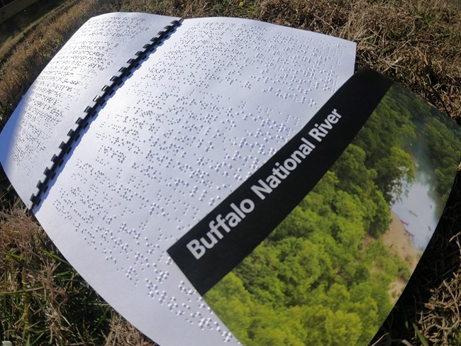 A park brochure rests on top of a booklet containing Braille.