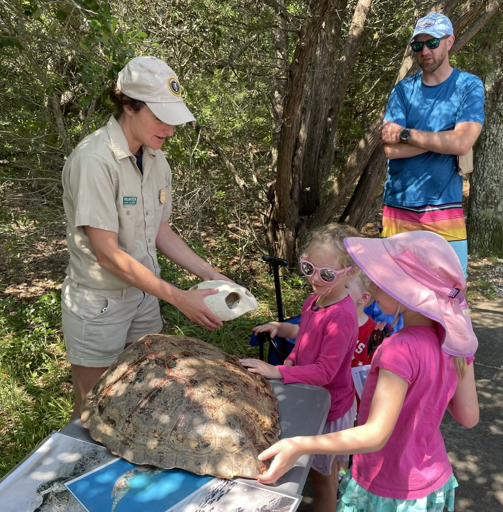 Volunteer holds a turtle skull while talking to young visitors.
