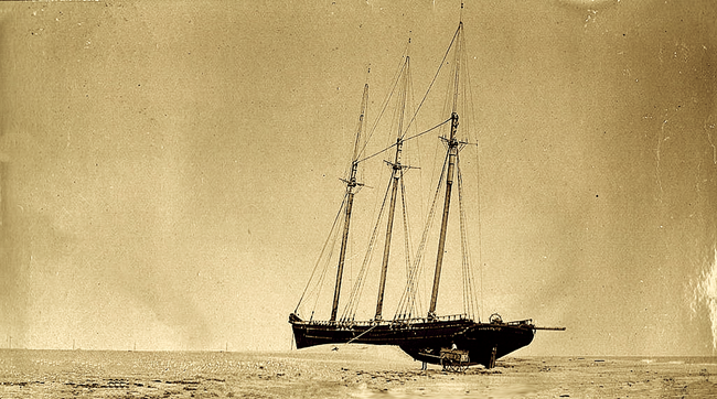 Sepia-toned photograph of three masted schooler wrecked on the beach.
