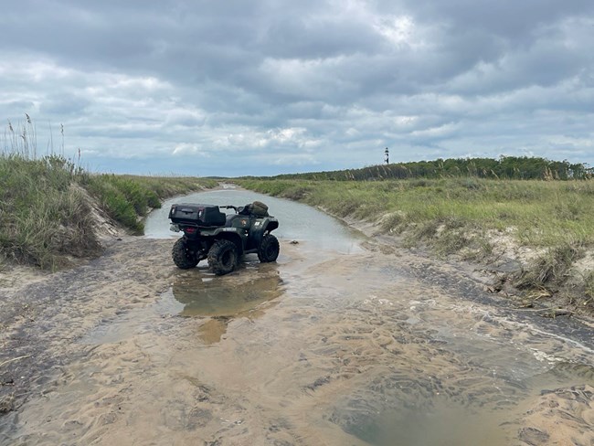 An ATV surrounded by water. Lighthouse in the background.
