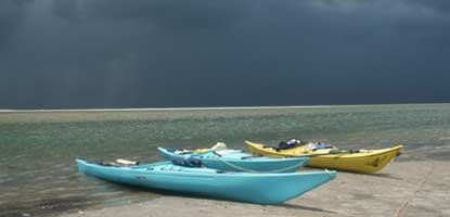Storm clouds gather across the sound from a group of kayaks pulled up on the beach.