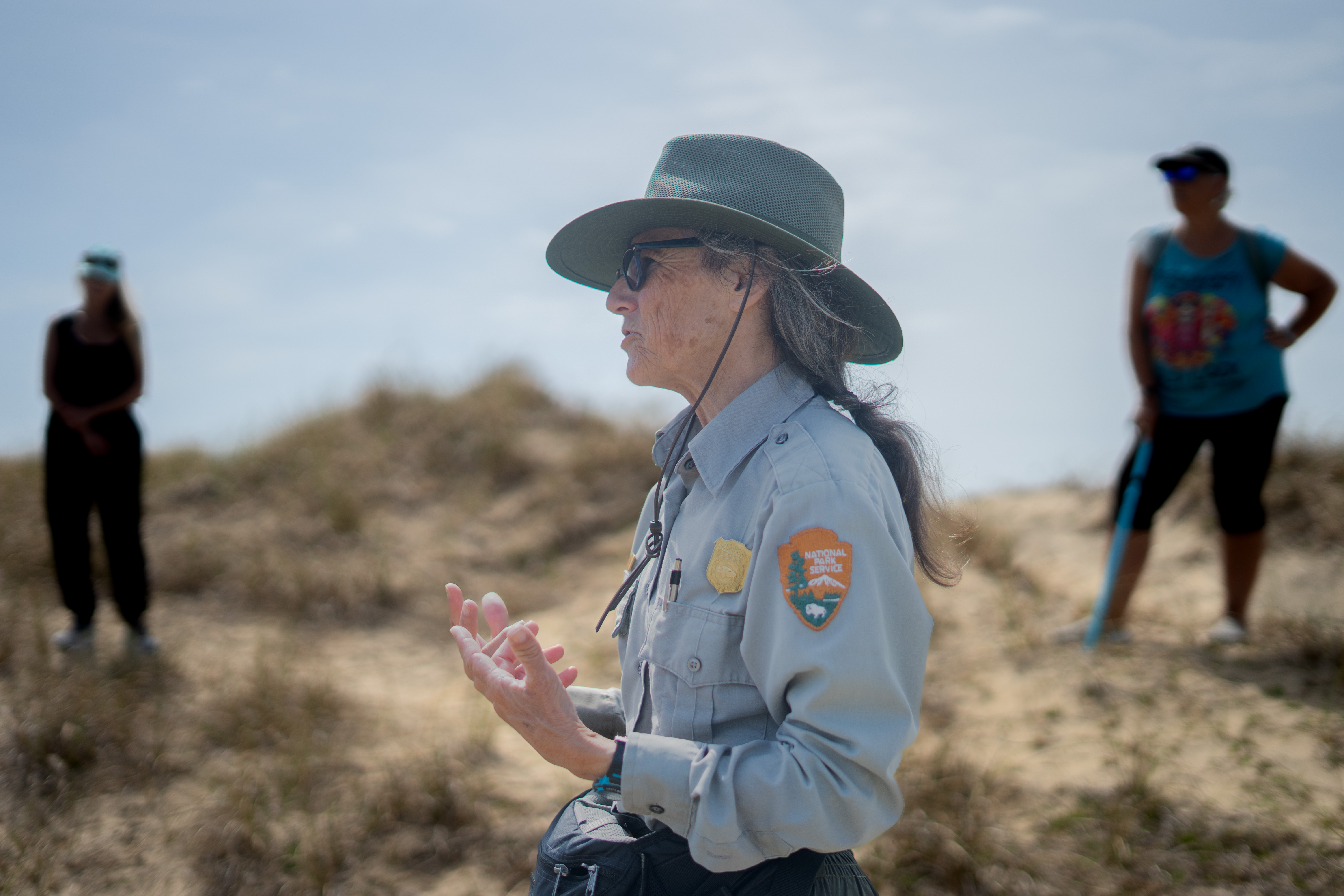 Dr. Sue, horse biologist, talks to people while standing on the dunes.