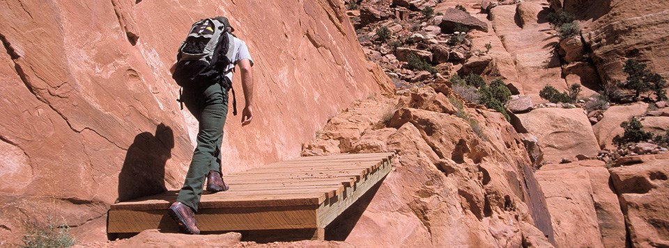 a man wearing a backpack hikes up a steep, rocky trail