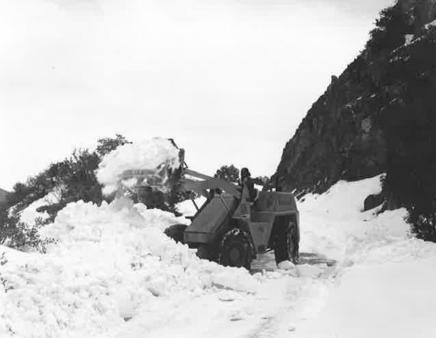 Black and white photo of snow removal on road using a backhoe.