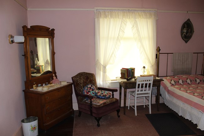 Pink bed room with vanity, table, chair, and bed.