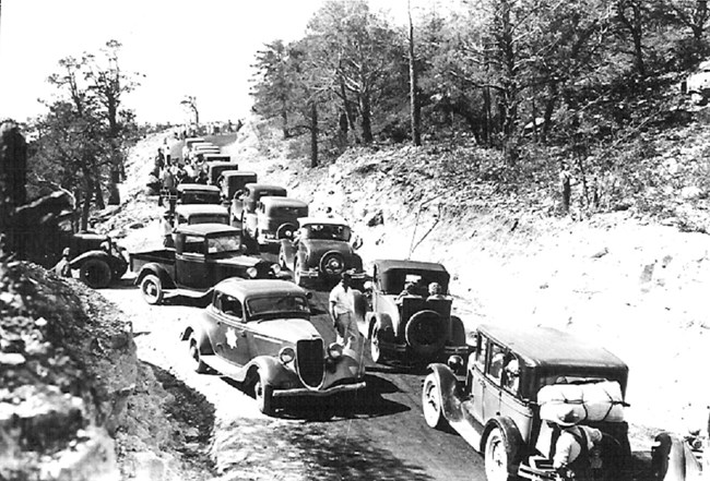 Black and white photo of narrow mountain road clogged with cars.