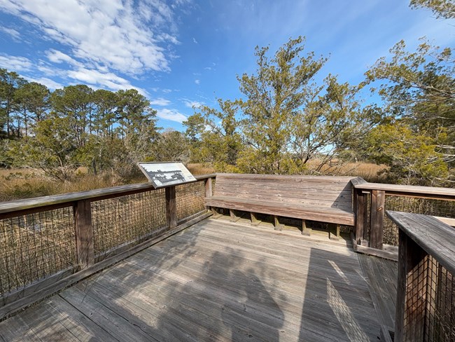 A boardwalk with a sign about the creek and a built-in wooden bench.