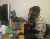 Two boys sit in front of a computer and work on their website projects.