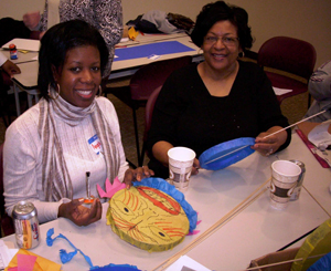 Two teachers create masks with construction paper and glue.