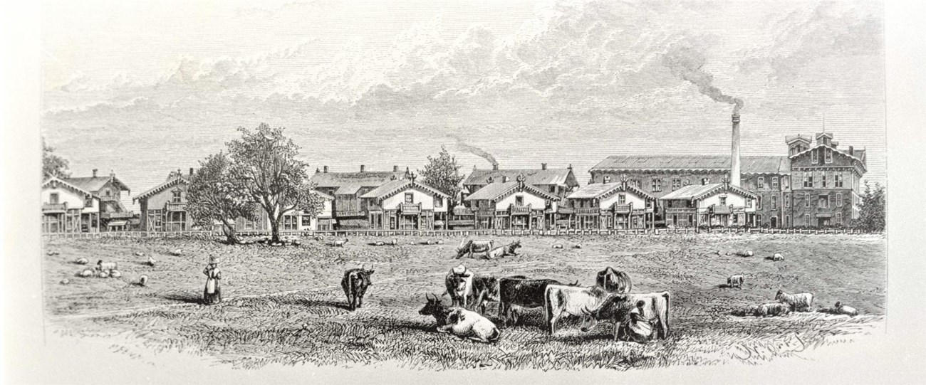 A factory in the background with people and cattle in the foreground in a grassy area.