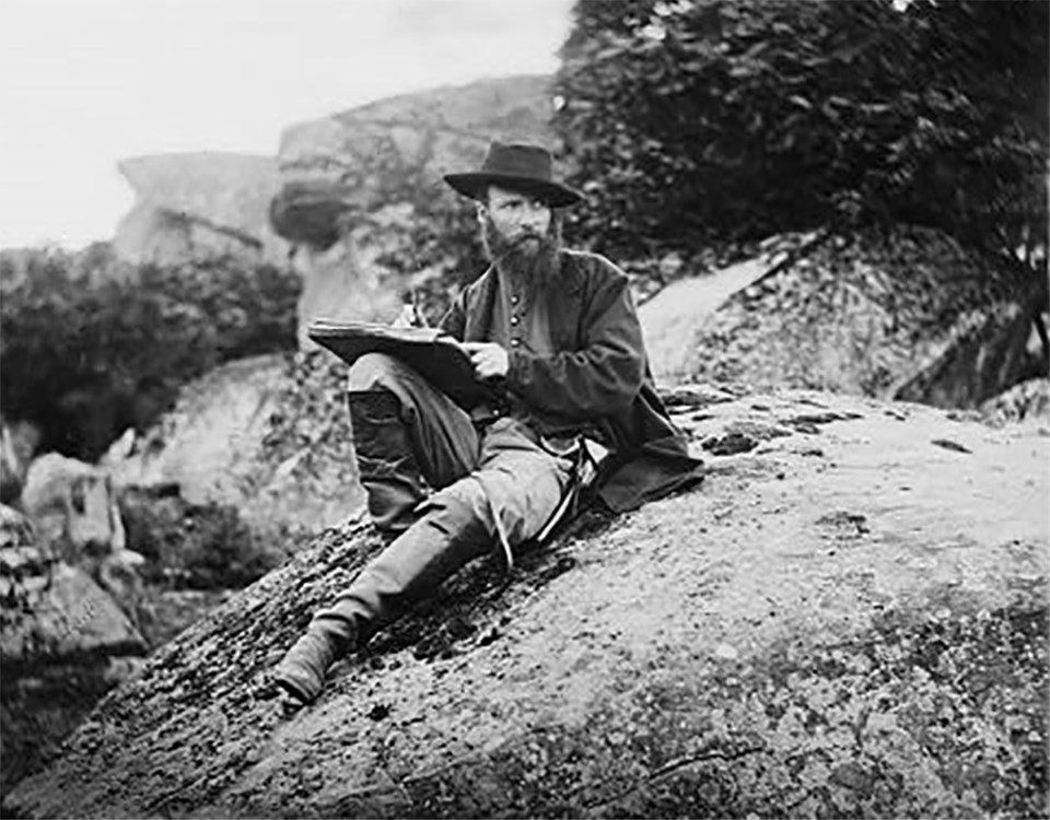 A Civil War sketch artist, Alfred Waud, sits atop a boulder in Devil's Den as he poses for a picture.