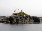 helicopter landing on a rocky island with a lighthouse