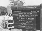 Two visitors pose by a sign for Faraway Ranch advertising horseback rides to see Chiricahua NM