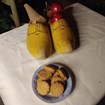 Four small round cookies sit on a plate. Next to them, large wooden shoes filled with apples. 