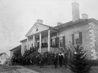 An 1883 photo captures men standing at the columned front of an antebellum style mansion.